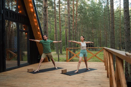 Man and woman practicing yoga outdoors on a wooden deck in a forest setting, enhancing wellness.