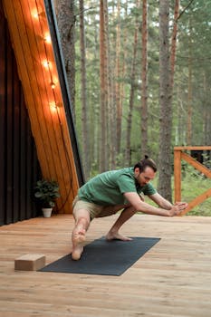 A man performs yoga on a wooden deck surrounded by trees, embodying peaceful balance.
