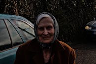 阴天，一位戴着围巾的老妇人站在汽车旁的户外肖像