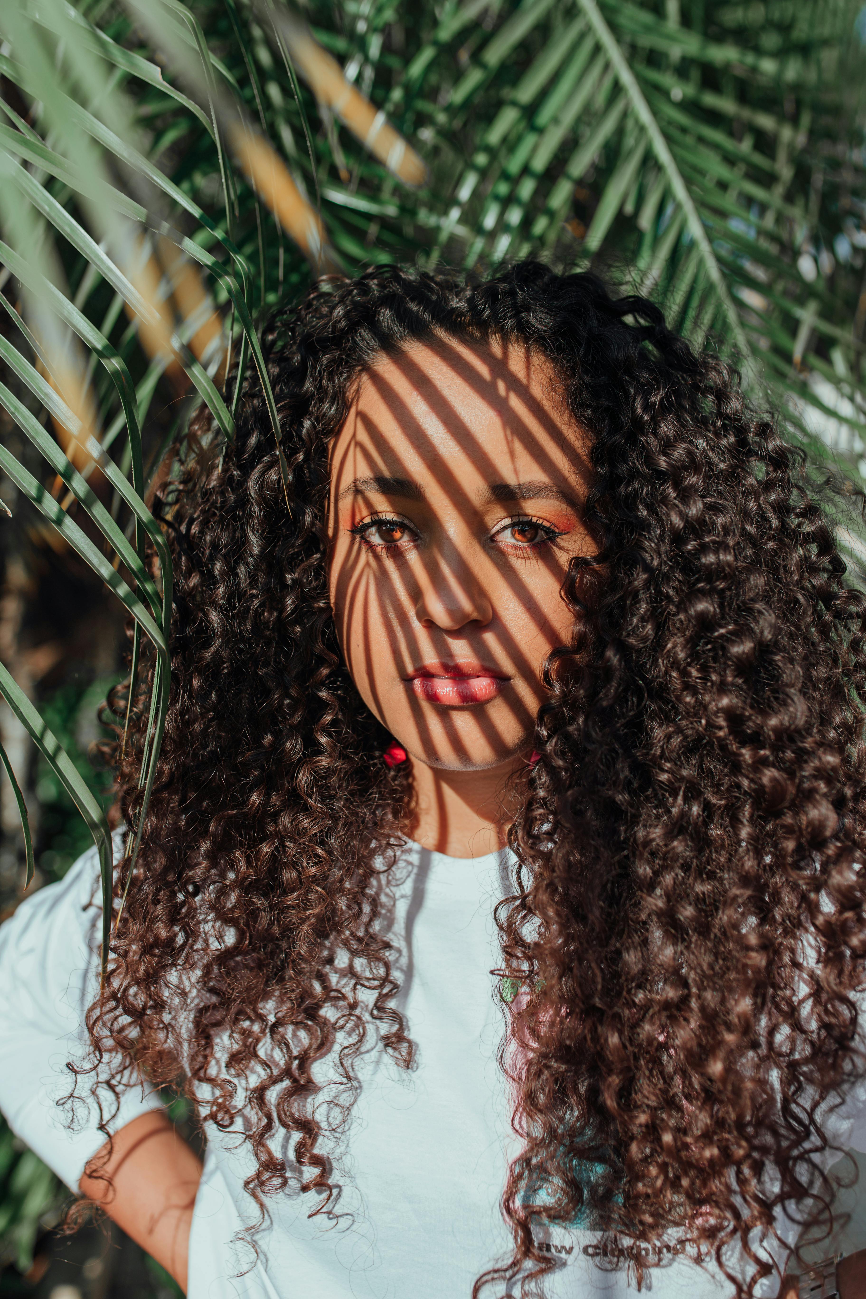 Portrait of a young woman with curly hair, sunlight casting shadows through leaves.