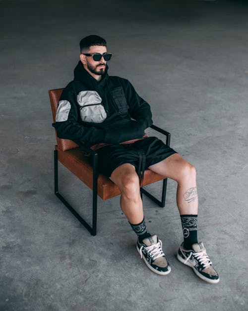 Man in Black Hoodie and Shorts Sitting on Chair