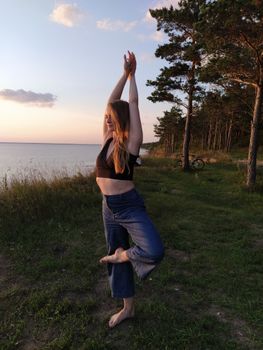 A woman performing a yoga pose outdoors by the sea, embracing a healthy lifestyle during sunset.