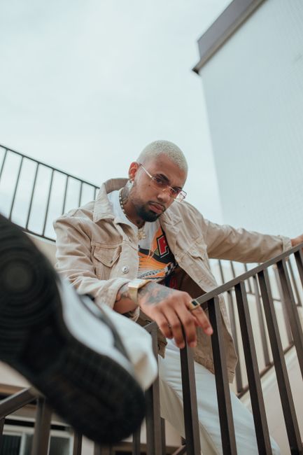 Young man in trendy outfit poses on an outdoor staircase with a modern urban backdrop.