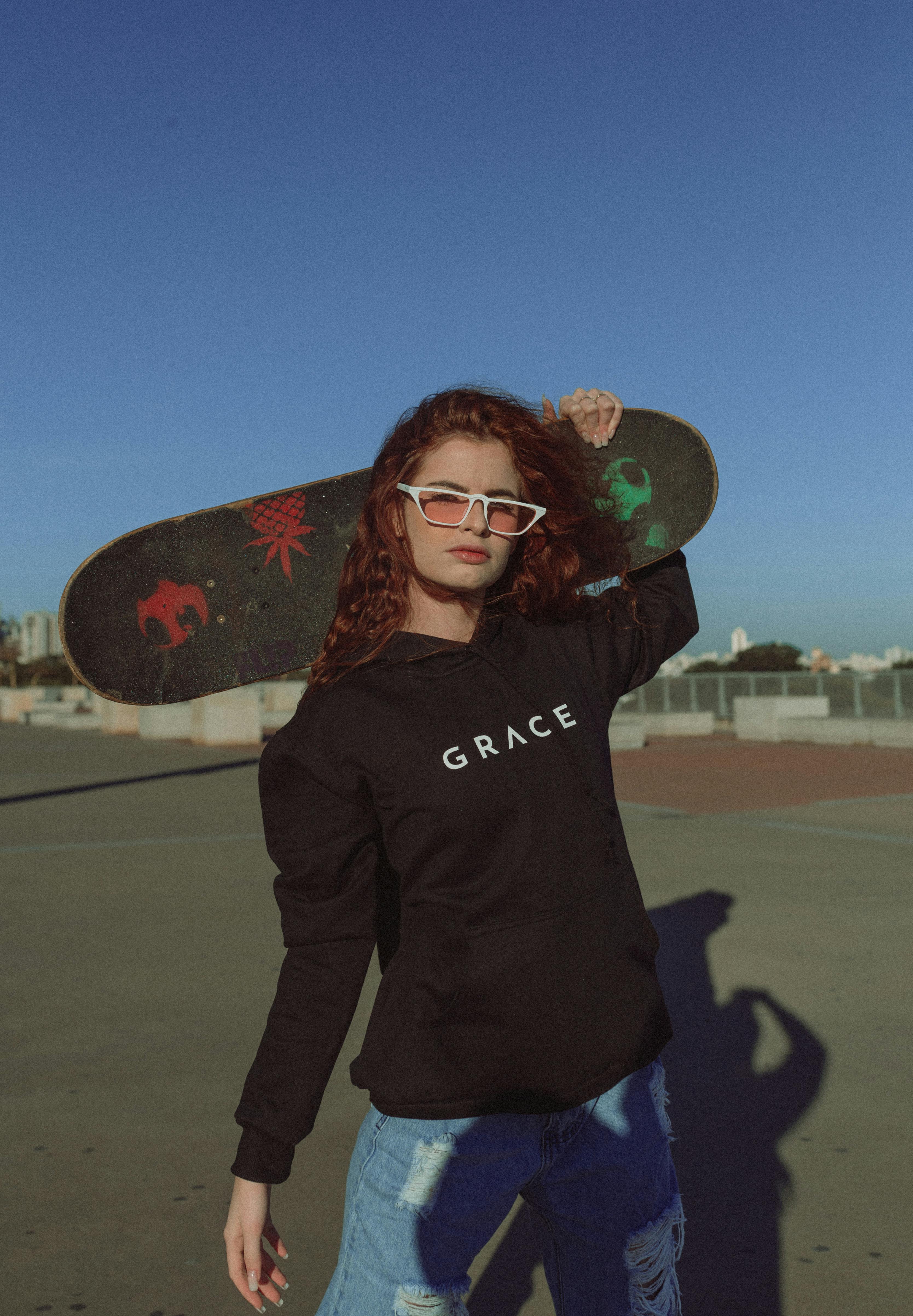 Confident skater girl with sunglasses and skateboard in urban setting on a sunny day.