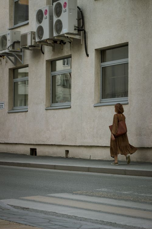Free A woman walks along a city sidewalk beside a building with air conditioners. Stock Photo