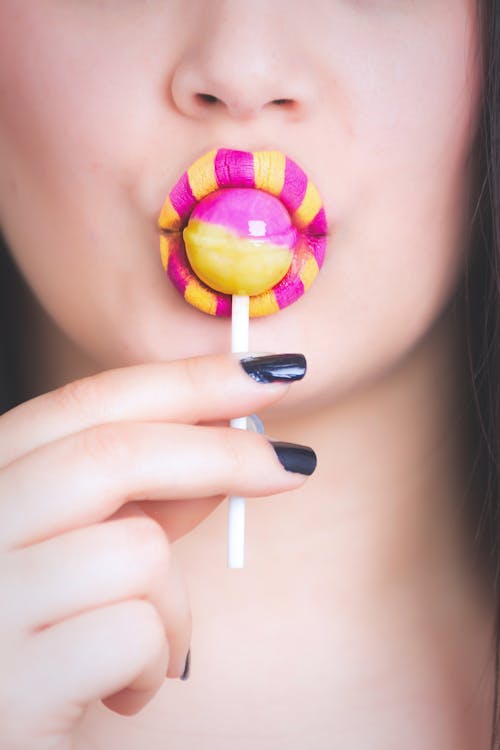 Free Woman Eating Pink and Yellow Lollipop Stock Photo