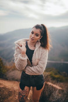 Young woman standing outdoors wearing a fleece jacket, showcasing a mountain landscape.