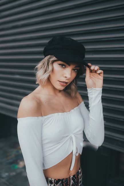 Portrait of a young fashionable woman posing confidently in a stylish outfit with a cap and crop top.