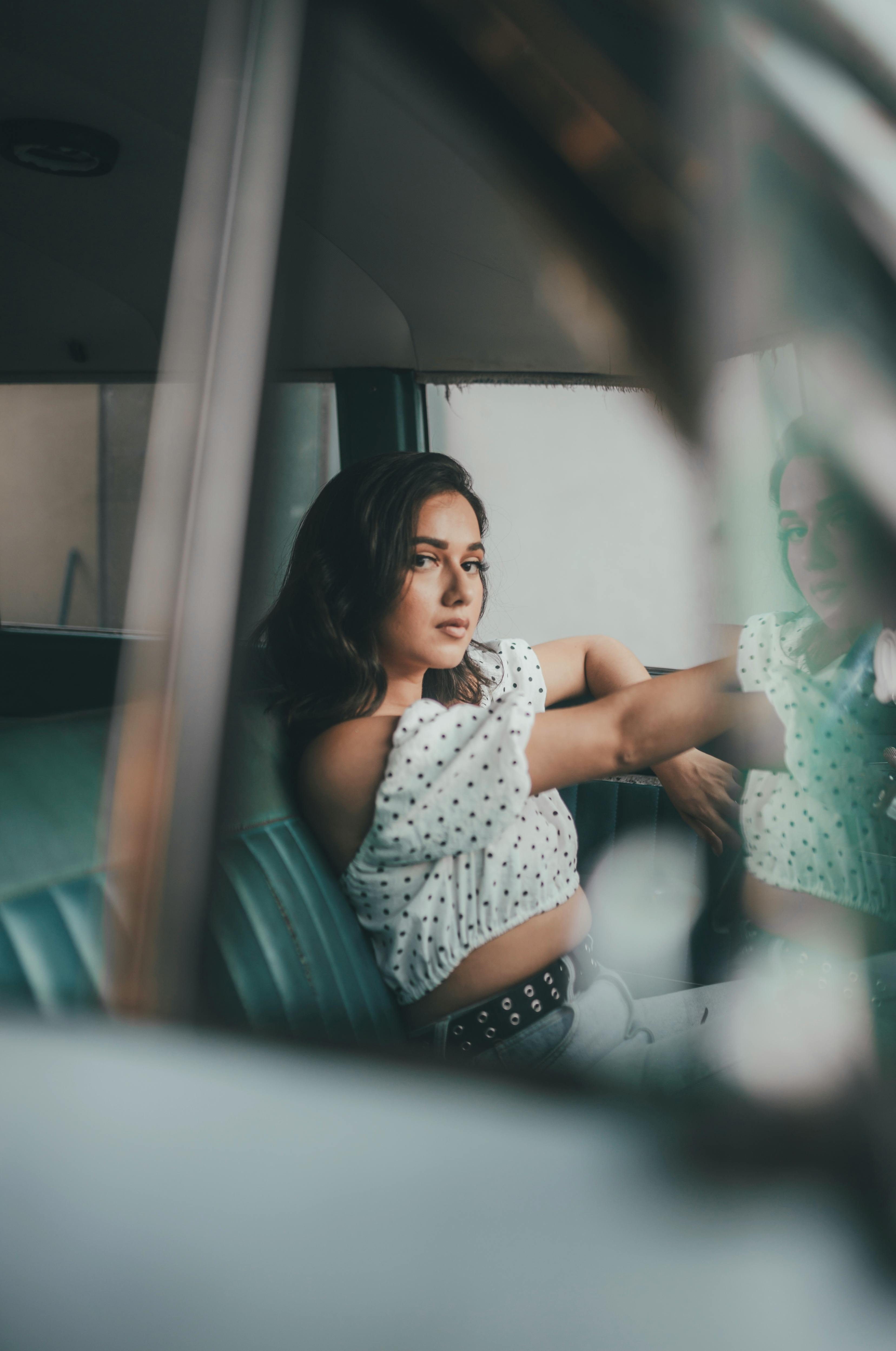 A young woman sits pensively in a vintage car, capturing a moment of introspection.