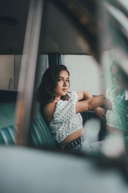 A young woman sits pensively in a vintage car, capturing a moment of introspection.