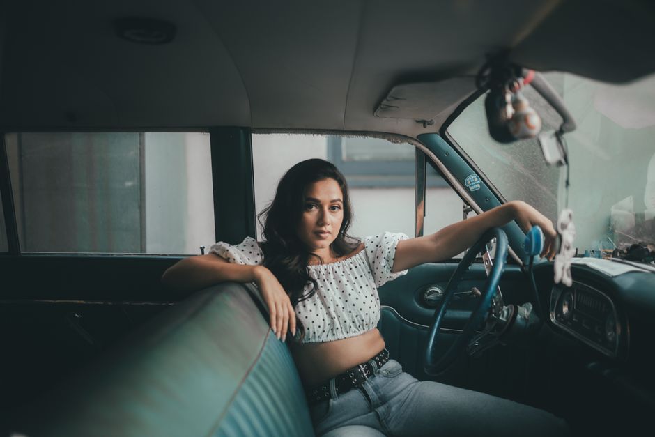 Young woman in a crop top poses inside a classic car, exuding confidence and style.