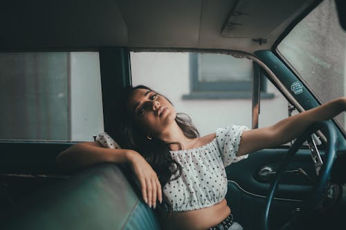 Woman in White and Black Polka Dot Crop Top Sitting on Driver Seat