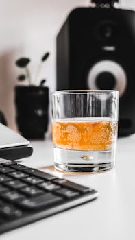 Close-up of a carbonated drink glass on a desk with a speaker in the background, providing a cozy indoor feel.