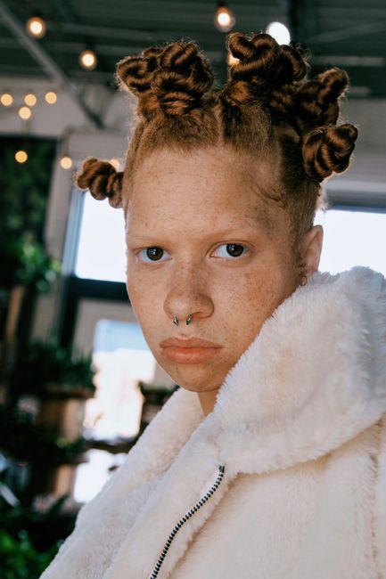 A striking modern portrait of a woman with unique hairstyle and a fur coat indoors.