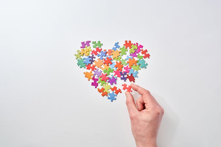 Person Placing A Puzzle On Heart Shaped Puzzle Pieces