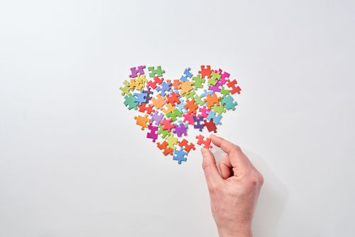 Free A hand arranges colorful jigsaw puzzle pieces into a heart shape on a white background. Stock Photo