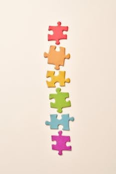 A stack of rainbow-colored puzzle pieces arranged vertically on a beige background.