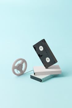 Minimalist composition of a retro VHS tape and film reel against a light blue background.