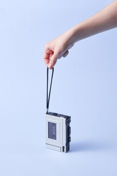 A vintage cassette player held by a hand against a light blue background, evoking retro vibes.