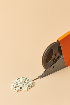 Retro film reel with scrabble tiles on a minimalist beige background, showcasing vintage charm.