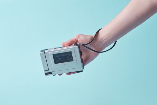 A hand holds a classic cassette player against a turquoise backdrop, highlighting retro technology.