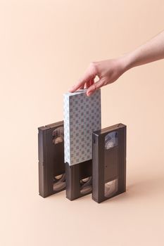 A hand placing a decorative VHS sleeve among vintage tapes on a neutral background.