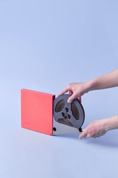 A person's hands holding a vintage audio tape reel on a purple studio background.