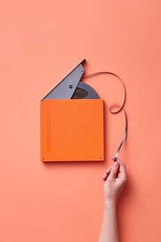 Hand holding a vintage film reel against a coral backdrop, showcasing retro vibes.