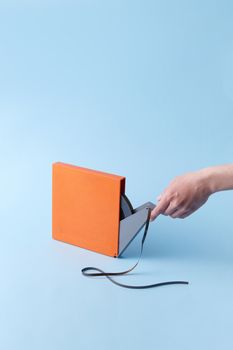 Close-up of a hand holding a vintage orange tape box against a blue background.