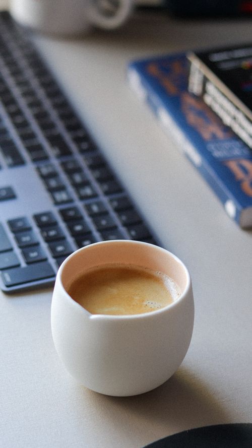 Free A cozy cup of coffee sits beside a keyboard on a desk, perfect for a productive work day. Stock Photo
