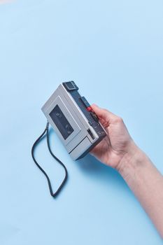Hand holding a classic cassette player on a pastel blue backdrop, evoking nostalgia.
