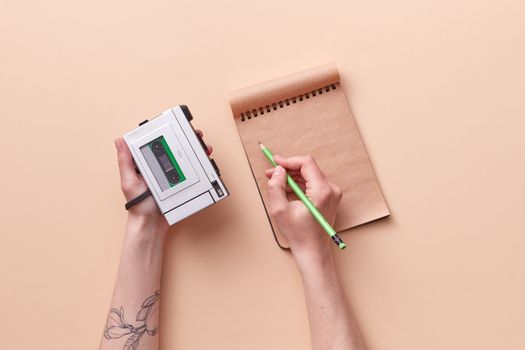 Vintage cassette player held in hand with notepad and pencil, on a minimalist pastel background.