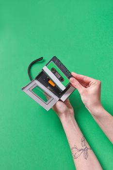 Close-up of hands holding a retro cassette tape against a vibrant green background.