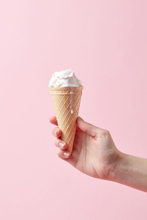 Free Close-up of a hand holding a vanilla ice cream cone with pink background. Stock Photo