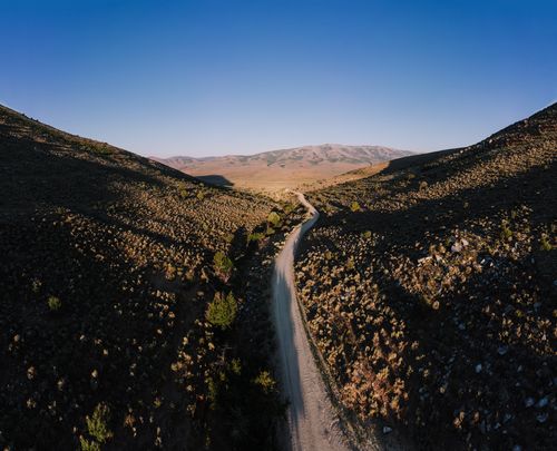 Free Aerial view of a winding road through a mountainous landscape under a clear blue sky. Stock Photo