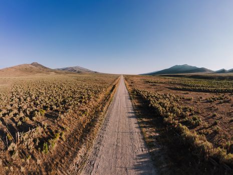 Stunning aerial shot of an unpaved road through a desert landscape with clear blue sky.