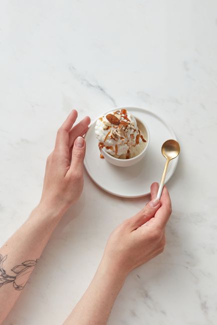 Three scoops of pale ivory dairy-free coconut ice cream in a chilled bowl, with visible flecks of vanilla bean and a metal scoop resting alongside.