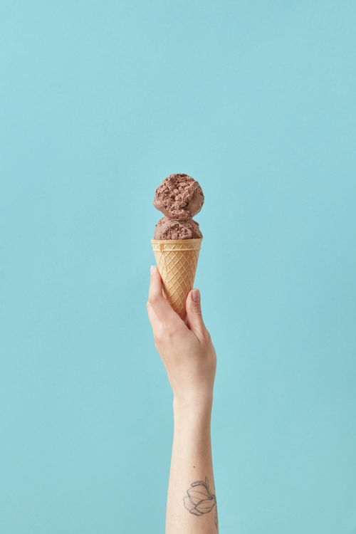 Free A tattooed hand holding a chocolate ice cream cone against a cyan background. Stock Photo