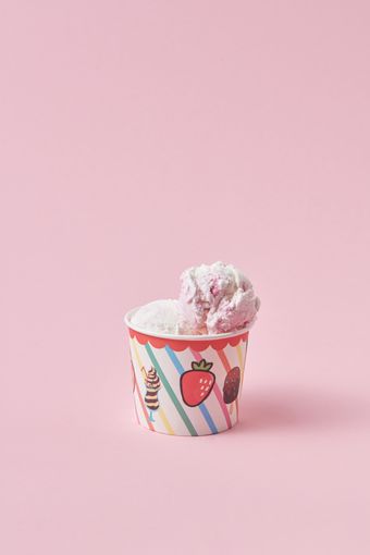 Scoop of strawberry ice cream in a striped paper cup on pink, photo by DS stories on Pexels