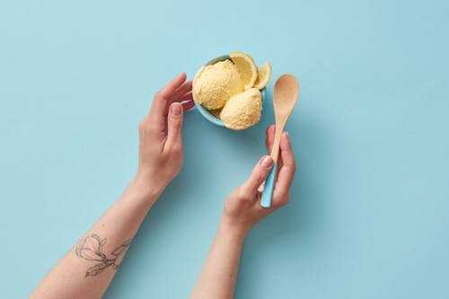 A Person Holding a Wooden Spoon Beside a Cup of Ice Cream with Lemon Slices