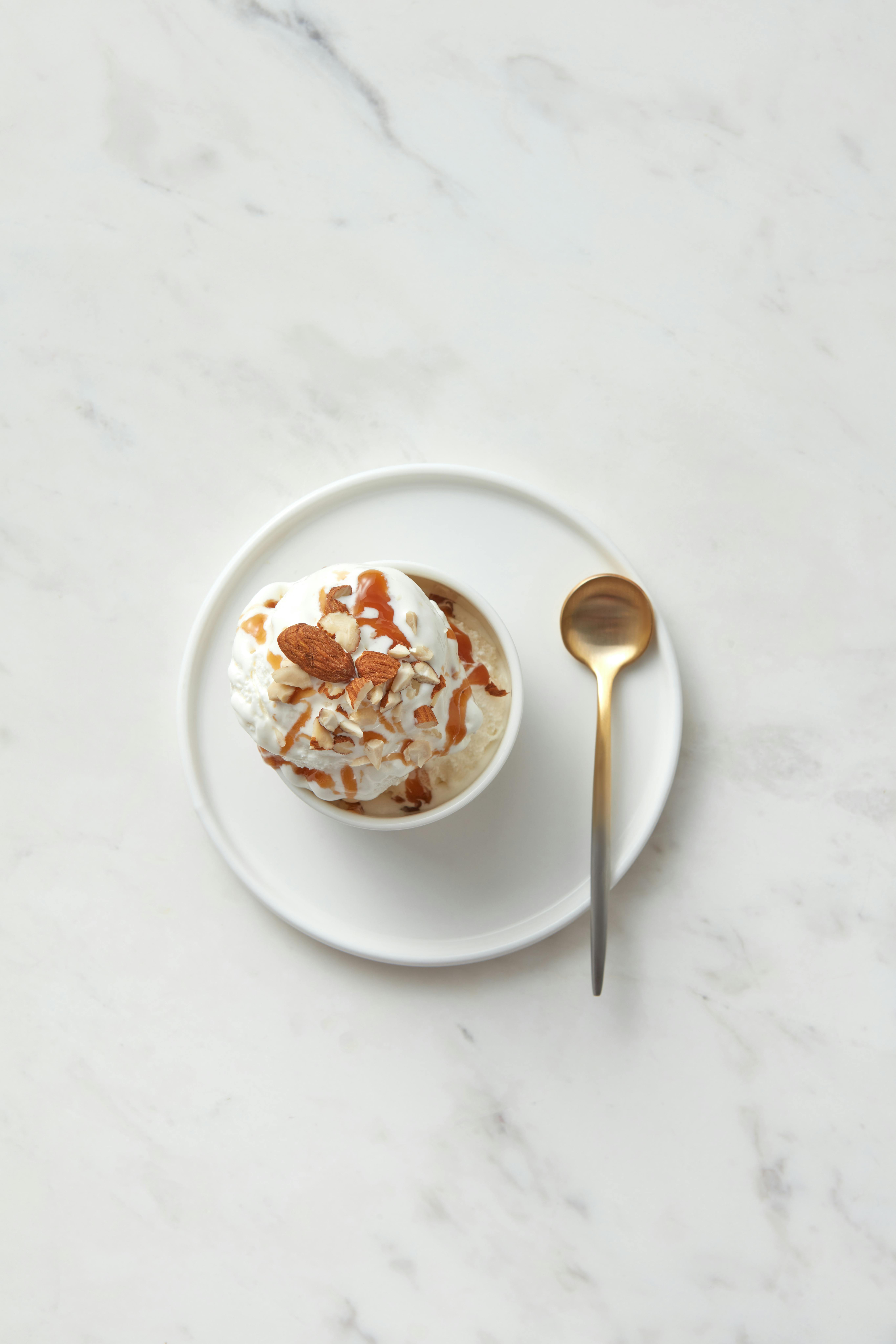 Flat lay of vanilla ice cream with caramel and nuts on a marble surface.