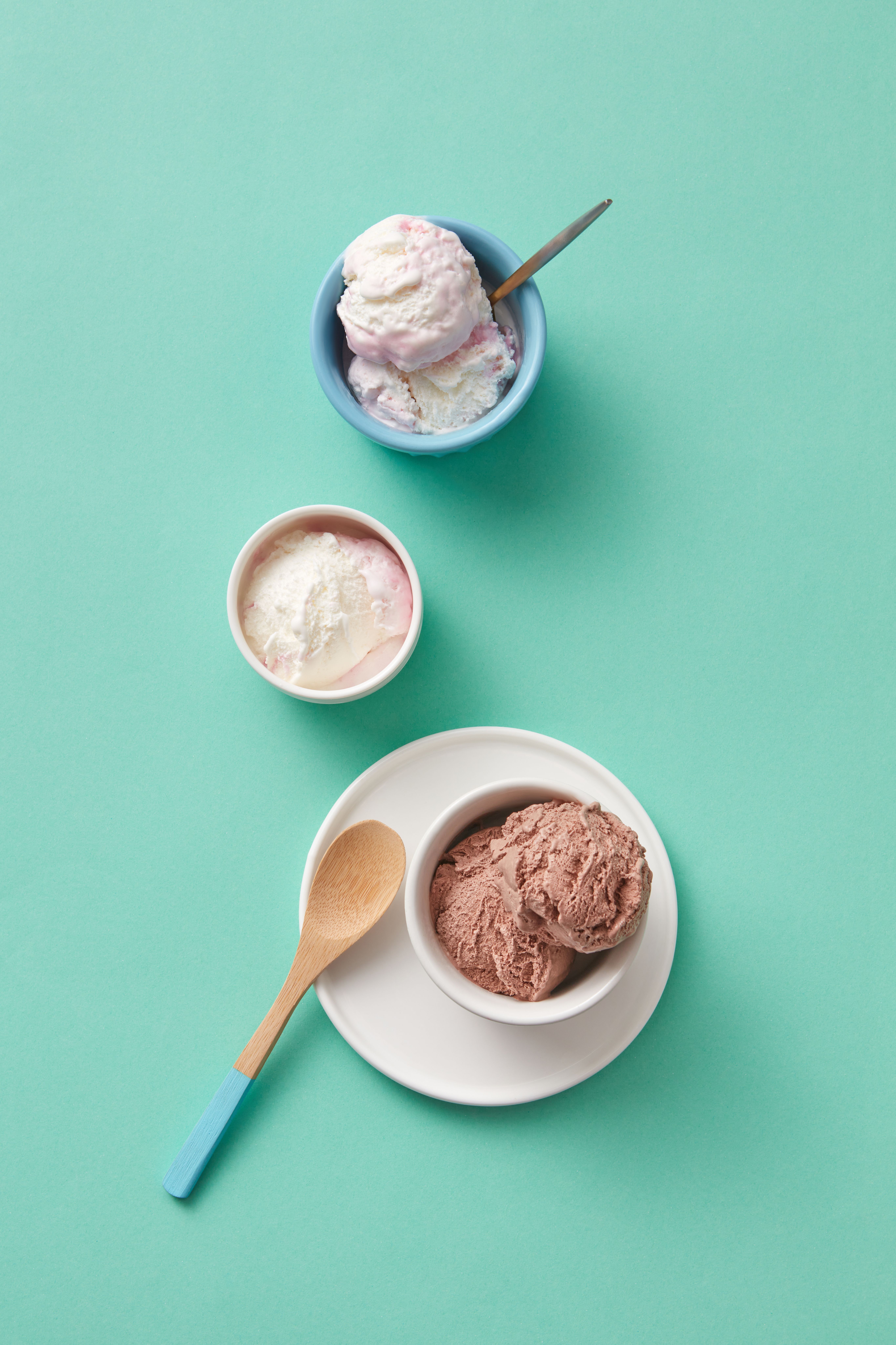 Assorted ice cream flavors in ceramic bowls on a turquoise background, featuring chocolate, vanilla, and berry.
