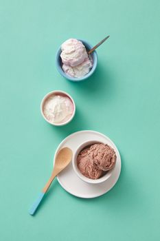 Assorted ice cream flavors in ceramic bowls on a turquoise background, featuring chocolate, vanilla, and berry.