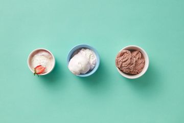 Three small bowls of strawberry, vanilla and chocolate ice cream on a mint green surface