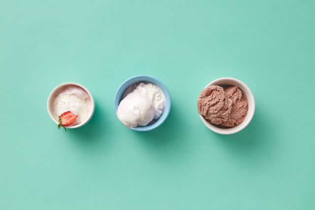 Three small bowls of strawberry, vanilla and chocolate ice cream on a mint green surface