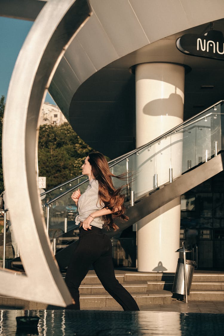 Stylish Woman Running On Pavement Against Contemporary Building In Town