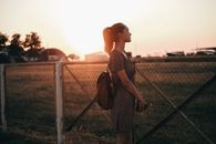 Contemplative woman with rucksack against aerodrome at sunset