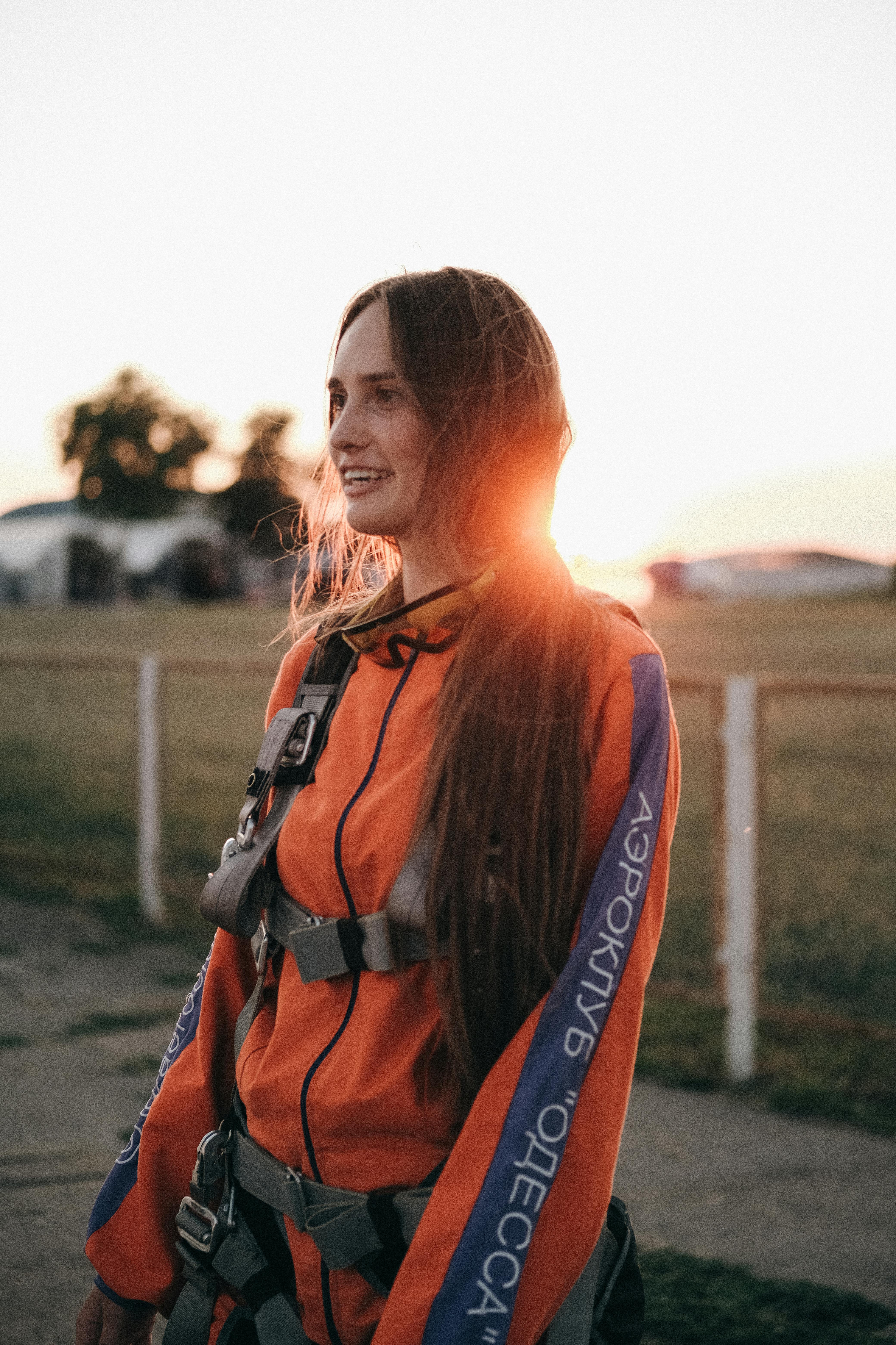 Content young female in parachuting jumpsuit looking forward against airfield in evening in back lit