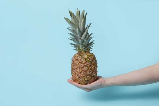 A hand holding a fresh pineapple against a solid blue background, evoking tropical freshness.