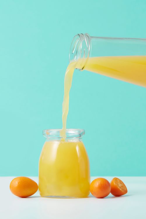 Free Vibrant orange juice being poured into a glass jar surrounded by fresh kumquats. Stock Photo